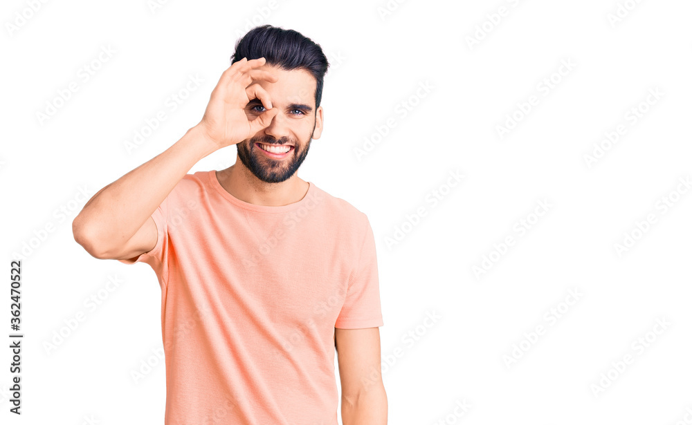 Young handsome man with beard wearing casual t-shirt doing ok gesture with hand smiling, eye looking through fingers with happy face. Young handsome man with beard wearing casual t-shirt doing ok gesture with hand smiling, eye looking through fingers with happy face.