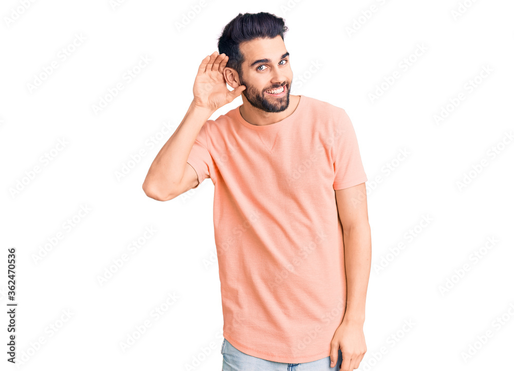 Young handsome man with beard wearing casual t-shirt smiling with hand over ear listening an hearing to rumor or gossip. deafness concept. Young handsome man with beard wearing casual t-shirt smiling with hand over ear listening an hearing to rumor or gossip. deafness concept.