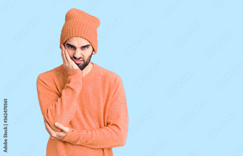 Young handsome man with beard wearing casual sweater and wool cap thinking looking tired and bored with depression problems with crossed arms.
