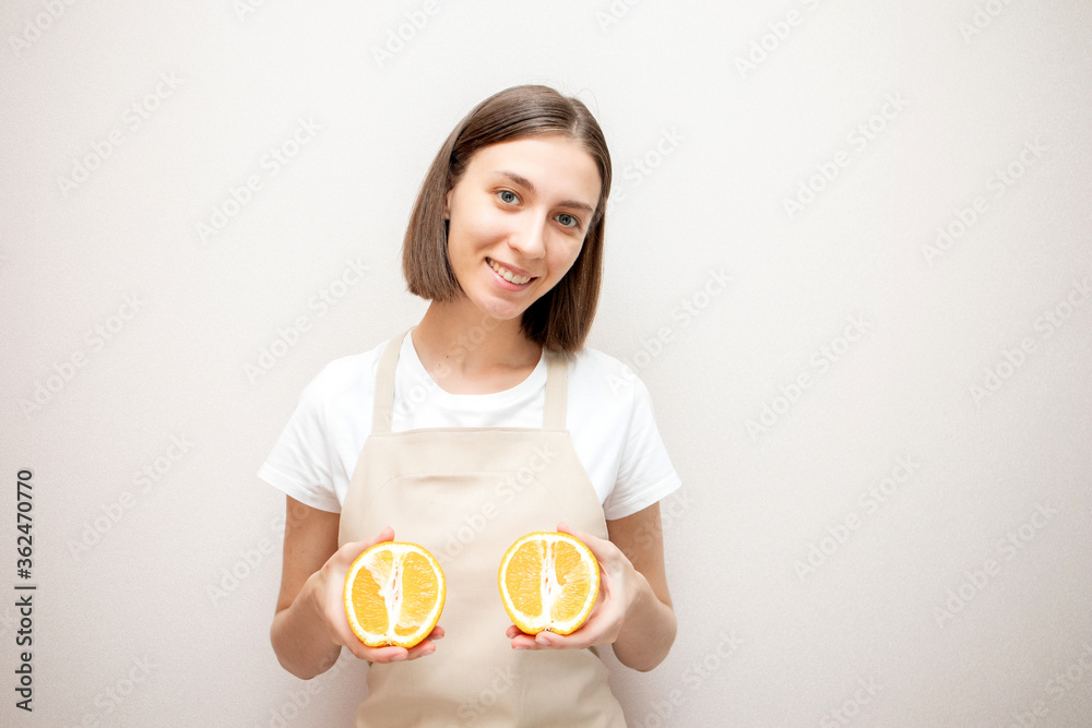 Smiling beautiful girl wearing apron holding two oranges. Woman in apron looking at camera and smiling. Smiling beautiful girl wearing apron holding two oranges. Woman in apron looking at camera and smiling.
