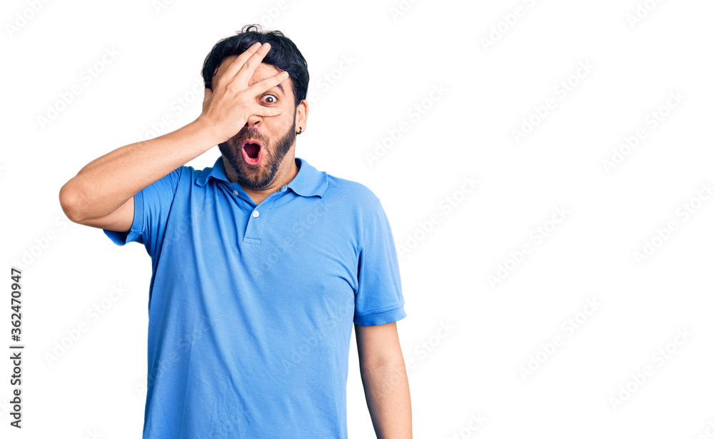 Young hispanic man wearing casual clothes peeking in shock covering face and eyes with hand, looking through fingers with embarrassed expression. Young hispanic man wearing casual clothes peeking in shock covering face and eyes with hand, looking through fingers with embarrassed expression.