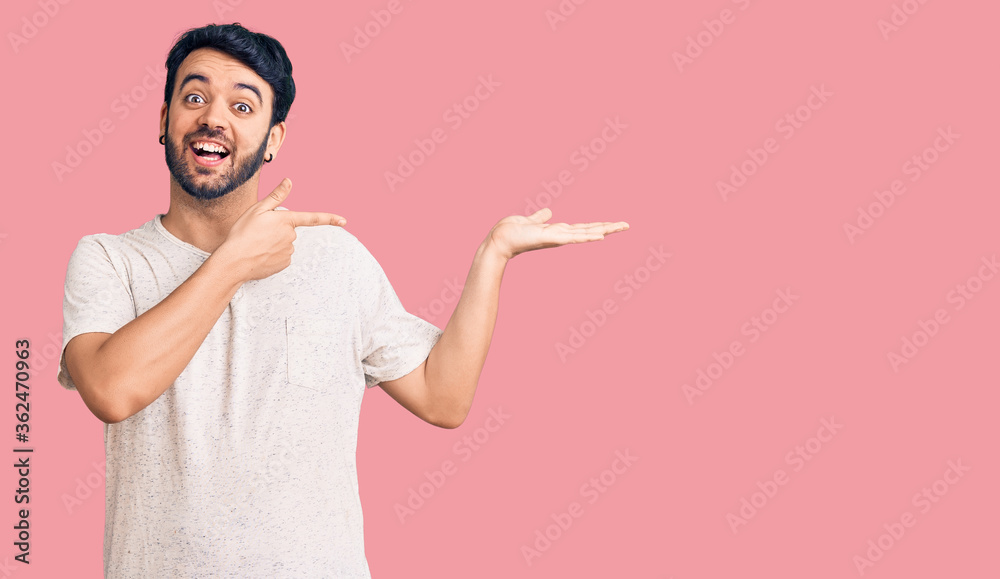 Young hispanic man wearing casual clothes amazed and smiling to the camera while presenting with hand and pointing with finger. Young hispanic man wearing casual clothes amazed and smiling to the camera while presenting with hand and pointing with finger.