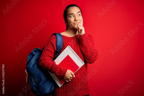 Young beautiful asian student woman wearing backpack standing over isolated red background serious face thinking about question, very confused idea © Krakenimages.com