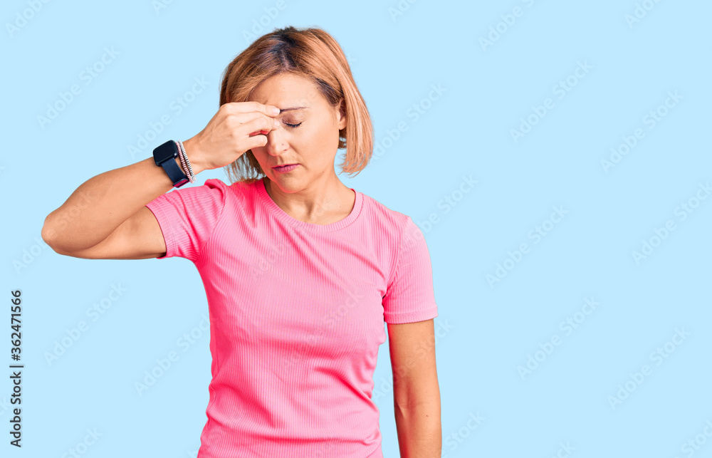 Young blonde woman wearing sportswear tired rubbing nose and eyes feeling fatigue and headache. stress and frustration concept. Young blonde woman wearing sportswear tired rubbing nose and eyes feeling fatigue and headache. stress and frustration concept.