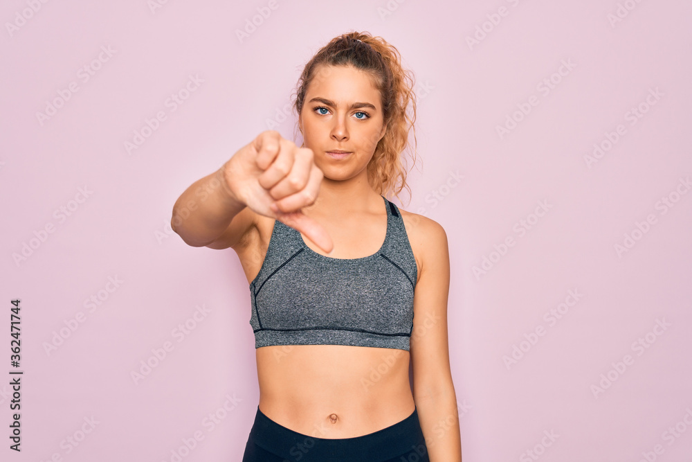 Young beautiful blonde sportswoman with blue eyes doing exercise wearing sportswear looking unhappy and angry showing rejection and negative with thumbs down gesture. Bad expression.