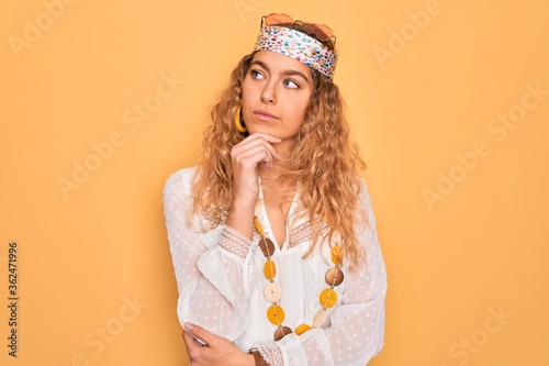 Young beautiful blonde hippie woman with blue eyes wearing sunglasses and accessories with hand on chin thinking about question  pensive expression. Smiling with thoughtful face. Doubt concept.