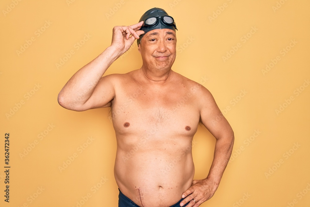 Middle age senior grey-haired swimmer man wearing swimsuit, cap and goggles worried and stressed about a problem with hand on forehead, nervous and anxious for crisis