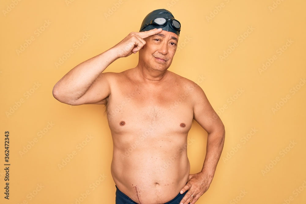Middle age senior grey-haired swimmer man wearing swimsuit, cap and goggles pointing unhappy to pimple on forehead, ugly infection of blackhead. Acne and skin problem Middle age senior grey-haired swimmer man wearing swimsuit, cap and goggles pointing unhappy to pimple on forehead, ugly infection of blackhead. Acne and skin problem