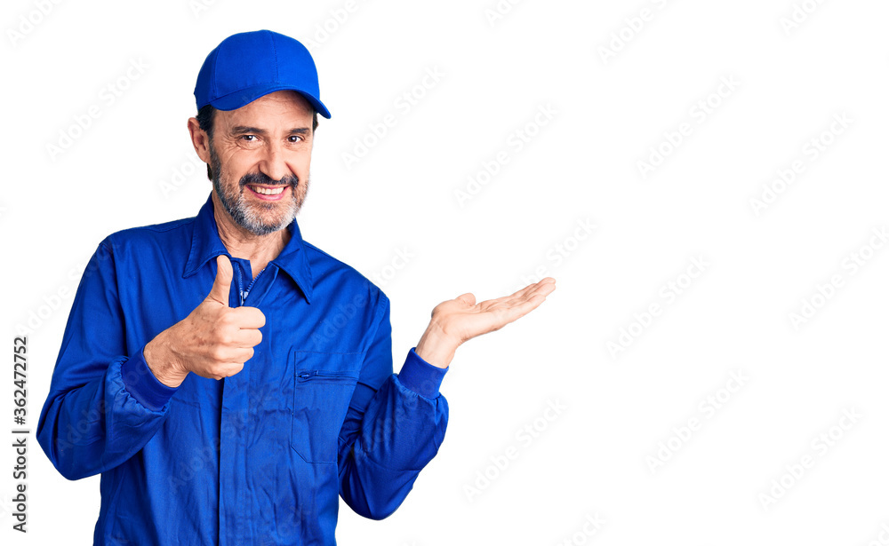 Middle age handsome man wearing mechanic uniform showing palm hand and doing ok gesture with thumbs up, smiling happy and cheerful