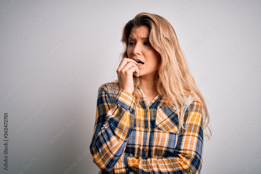 Young beautiful blonde woman wearing casual shirt standing over isolated white background looking stressed and nervous with hands on mouth biting nails. Anxiety problem. Young beautiful blonde woman wearing casual shirt standing over isolated white background looking stressed and nervous with hands on mouth biting nails. Anxiety problem.