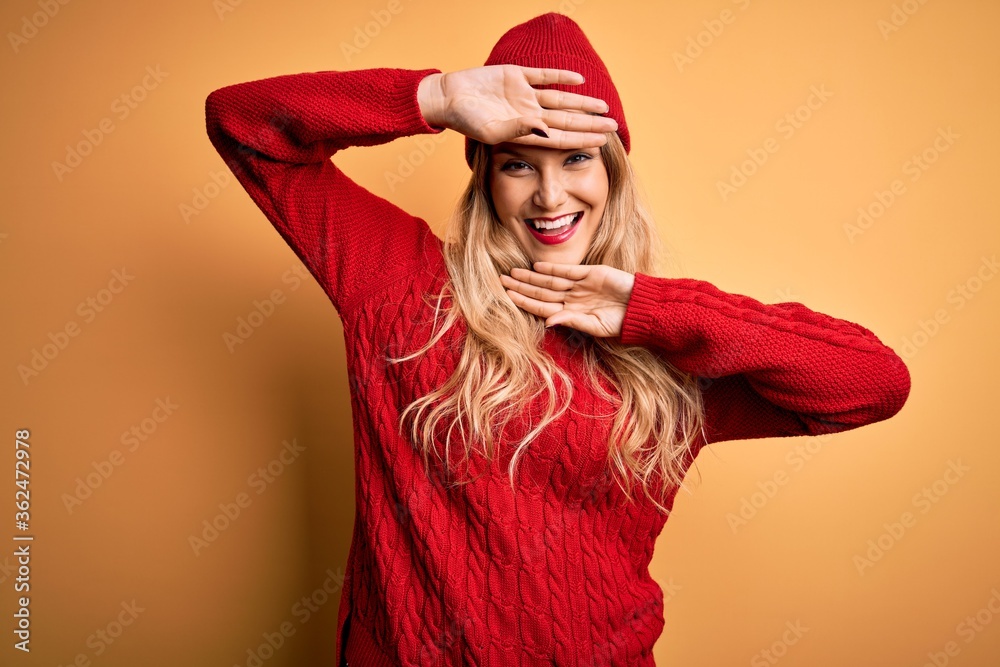 Young beautiful blonde woman wearing casual sweater and wool cap over white background Smiling cheerful playing peek a boo with hands showing face. Surprised and exited Young beautiful blonde woman wearing casual sweater and wool cap over white background Smiling cheerful playing peek a boo with hands showing face. Surprised and exited