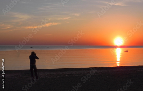 Back view of a silhouette of a man photographing the sun at sunset on the beach on holidays