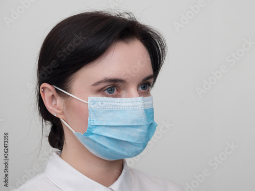 Portrait of a young European woman in a protective disposable medical mask. Concept of caronavirus Cavid 19 and human quarantine. Girl in a mask on a white wall. Masked medical worker.