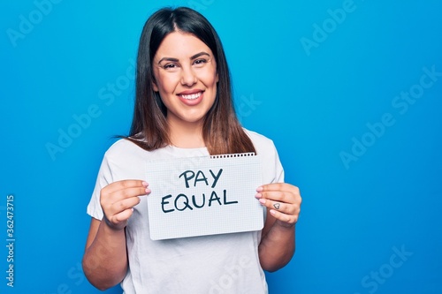 Young beautiful woman asking for gender equality holding paper with pay equal message looking positive and happy standing and smiling with a confident smile showing teeth
