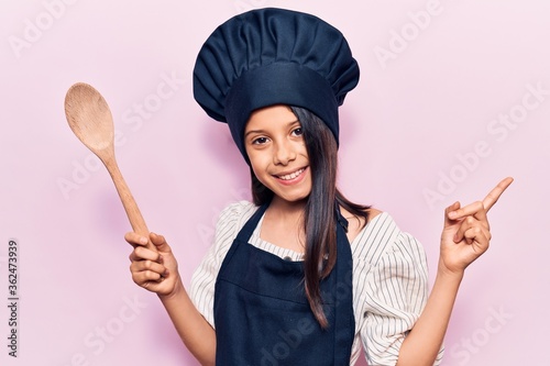 Canvas Print Beautiful child girl wearing cooker uniform smiling happy pointing with hand and