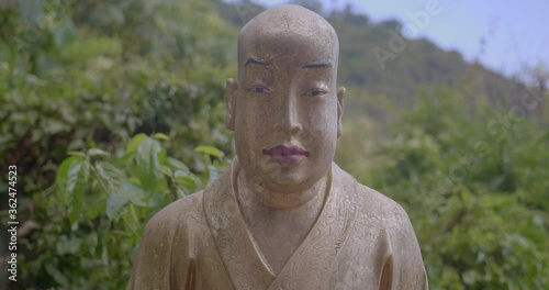 Beautiful golden buddha statue looking at the camera. It is bald and has a long vertical face. Steady professional 4k shot. High dynamic range footage. photo