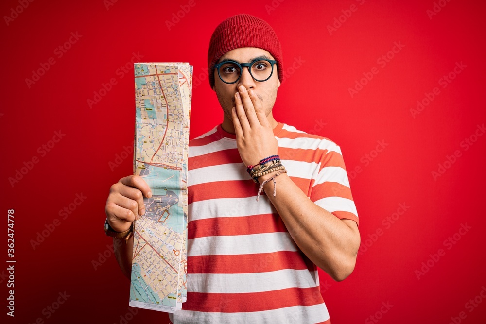Obraz na plátně Young brazilian tourist man on vacation holding city map over isolated red backg