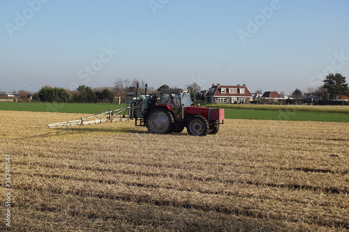 Tractor with a crop protection sprayer in the field with flower bulbs, covered with straw in winter as protection against frost damage and the sandy soil will not drift away. Egmond, Netherlands, 2020 photo