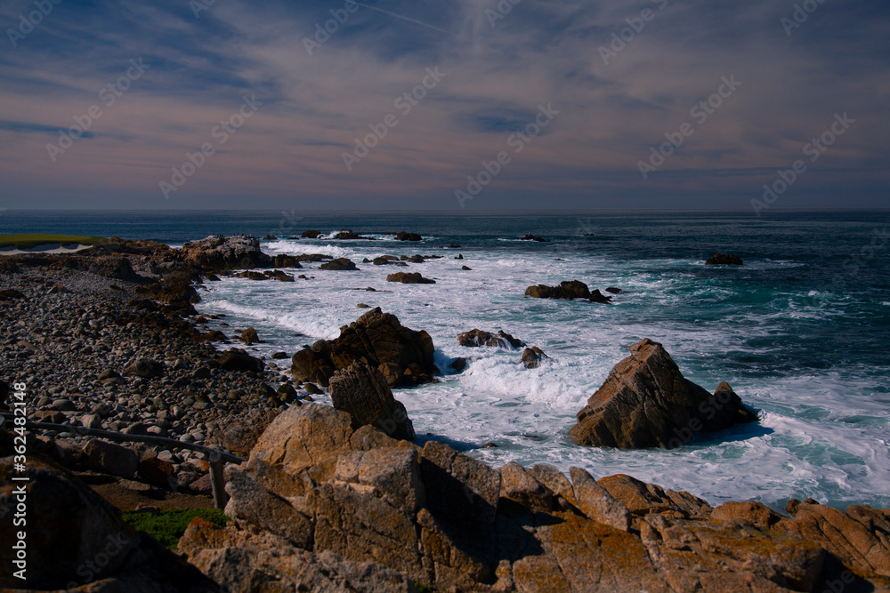 A rocky coastal landscape taken at a location near Point Lobos National Park in Northern California. Powerful waves of the Pacific Ocean are hitting on the rocks creating spectacular splashes.