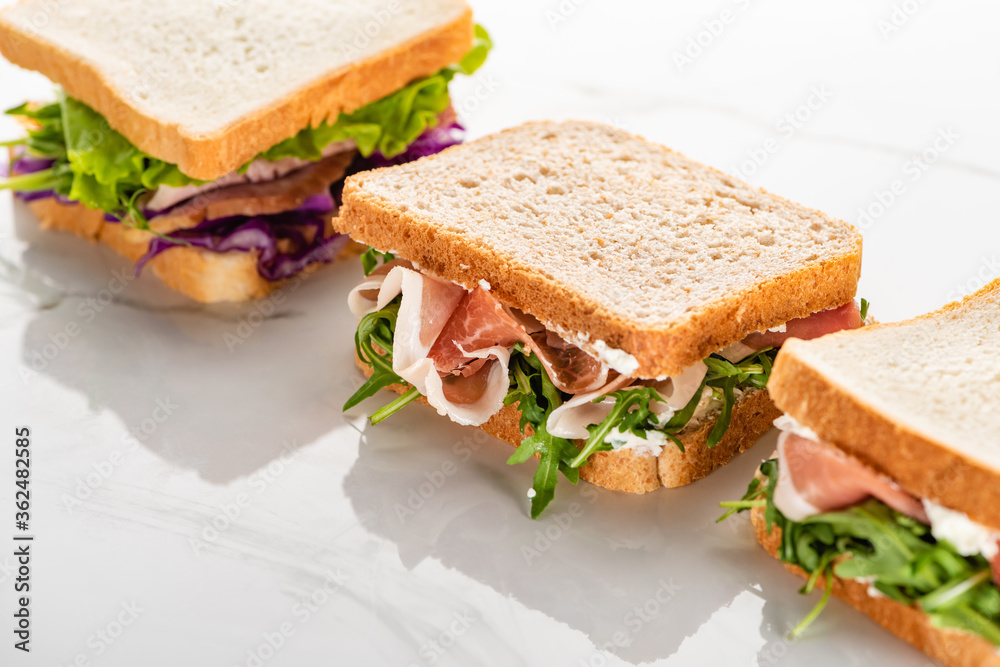 fresh sandwiches with arugula and meat on white marble surface fresh sandwiches with arugula and meat on white marble surface