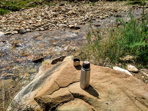 Coffee with milk and thermos on a rock near a mountain river.