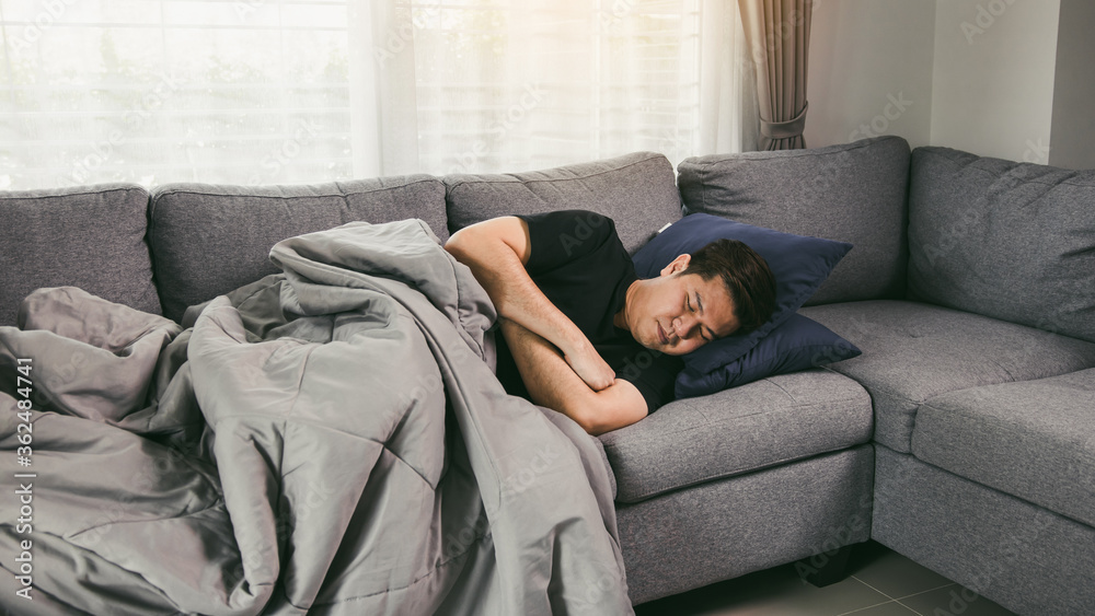 Asian man feel the illness while he was cold lying on the sofa and wearing a blanket at his house. Asian man feel the illness while he was cold lying on the sofa and wearing a blanket at his house.