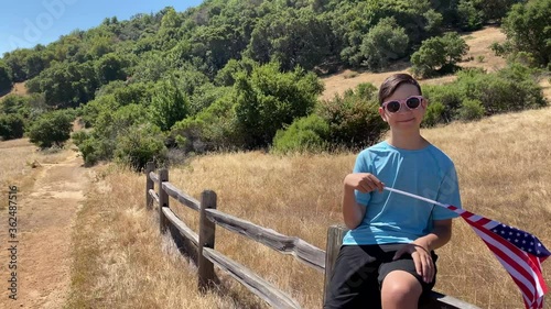 Wallpaper Mural A teenage boy sits on a wood fence and waves the USA flag. Hiking trail in the park, summer, hot sunny day. Green background. Boy smiles. California, US Torontodigital.ca