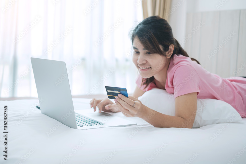Happy woman holding credit card and using computer laptop for online shopping while making orders on bed in morning at home. Business, technology, ecommerce, digital banking and online payment concept Happy woman holding credit card and using computer laptop for online shopping while making orders on bed in morning at home. Business, technology, ecommerce, digital banking and online payment concept