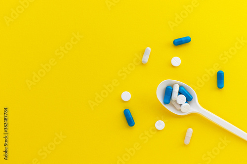 Plastic spoon with pills and capsules on yellow background. Pharmaceutical industry. Epidemic, painkillers, healthcare and treatment concept. Flat lay. Top view with copy space.
