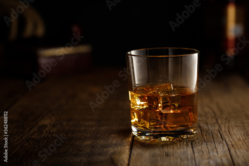 Glass of whiskey with ice on wooden table. Copy space for text.