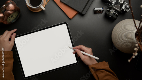 Female worker using blank screen tablet with stylus on dark luxury office desk with camera, supplies and decoration photo