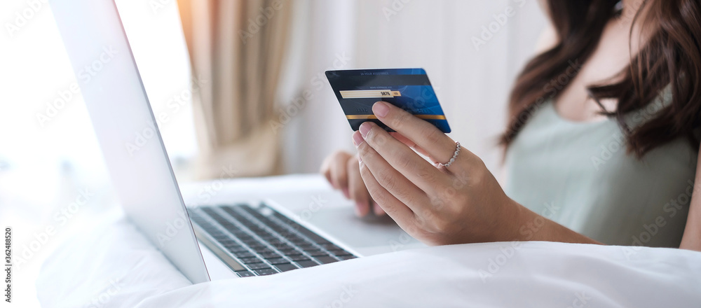 Happy woman holding credit card and using computer laptop for online shopping while making orders on bed in morning at home. Business, technology, ecommerce, digital banking and online payment concept Happy woman holding credit card and using computer laptop for online shopping while making orders on bed in morning at home. Business, technology, ecommerce, digital banking and online payment concept