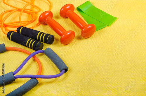 Sport, fitness concept, healthy lifestyle, women's sports of set Fitness concepts with equipment skipping rope, dumbbell, fitness expander, water bottle and towel on yellow background.