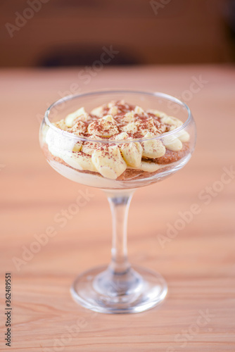 Delicious tiramisu dessert served in tall glass over rustic wooden background. Traditional Italian dessert.