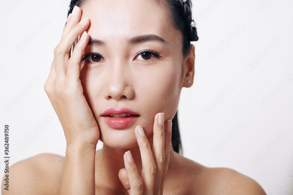 Beautiful young Asian woman touching her face and looking at camera Beautiful young Asian woman touching her face and looking at camera