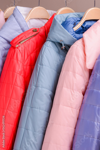 New collection of down jackets on hangers in the market. Colorful background of modern spring, autumn outerwear.