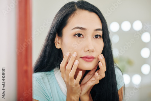 Young Asian woman looking at herself in mirror and checking if she has any wrinkles