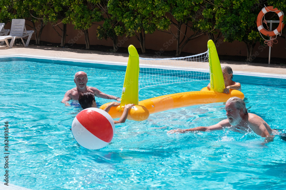 Senior happy couples in  activity in swimming pool - four people friends or family enjoying vacation with balloon and volleyball in water