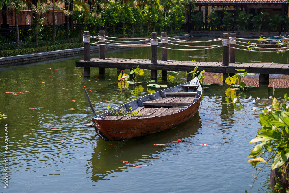 Obraz premium Wooden boat on the pond near the pier in a tropical garden in Danang, Vietnam