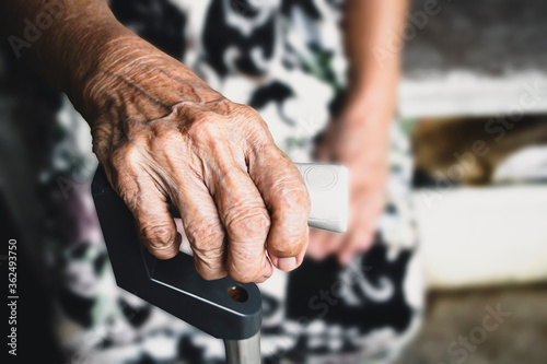 The hands of an elderly woman have curly fingers and wrinkled, holding the old cane sitting alone.