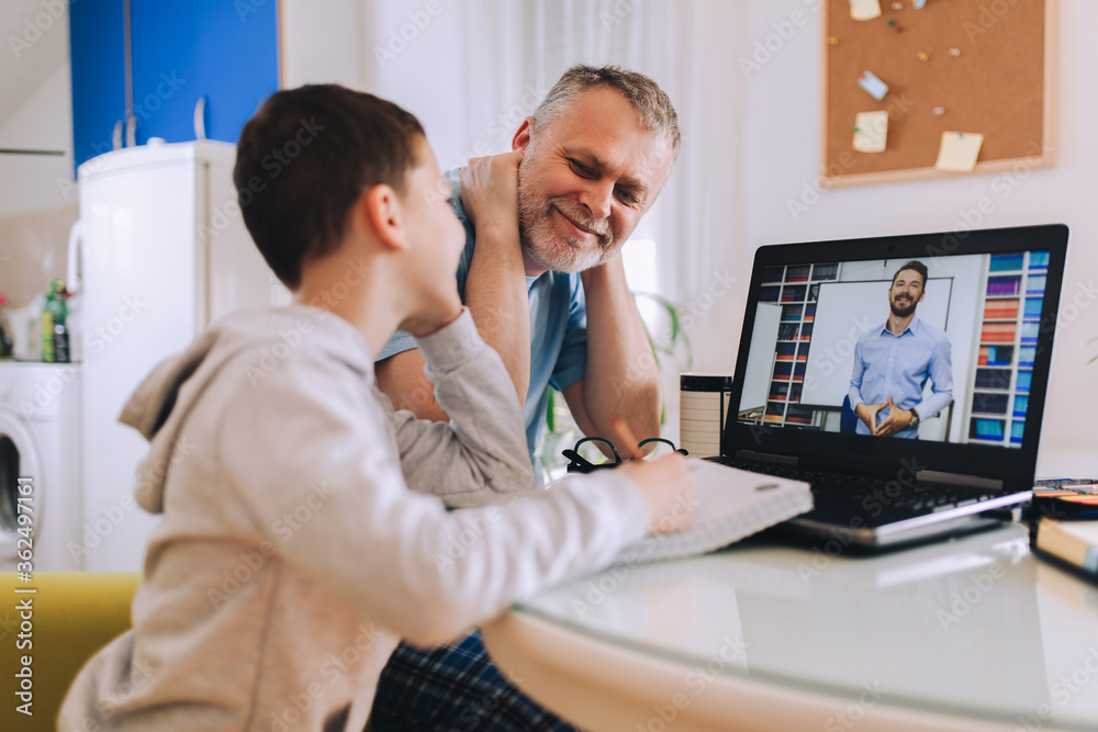 Schoolboy educate online. Father helps his son with home work. Boy in video conference with teacher on laptop at home.
