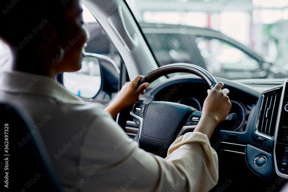rear view on young african woman sitting behind the wheel of automobile in cars showroom rear view on young african woman sitting behind the wheel of automobile in cars showroom