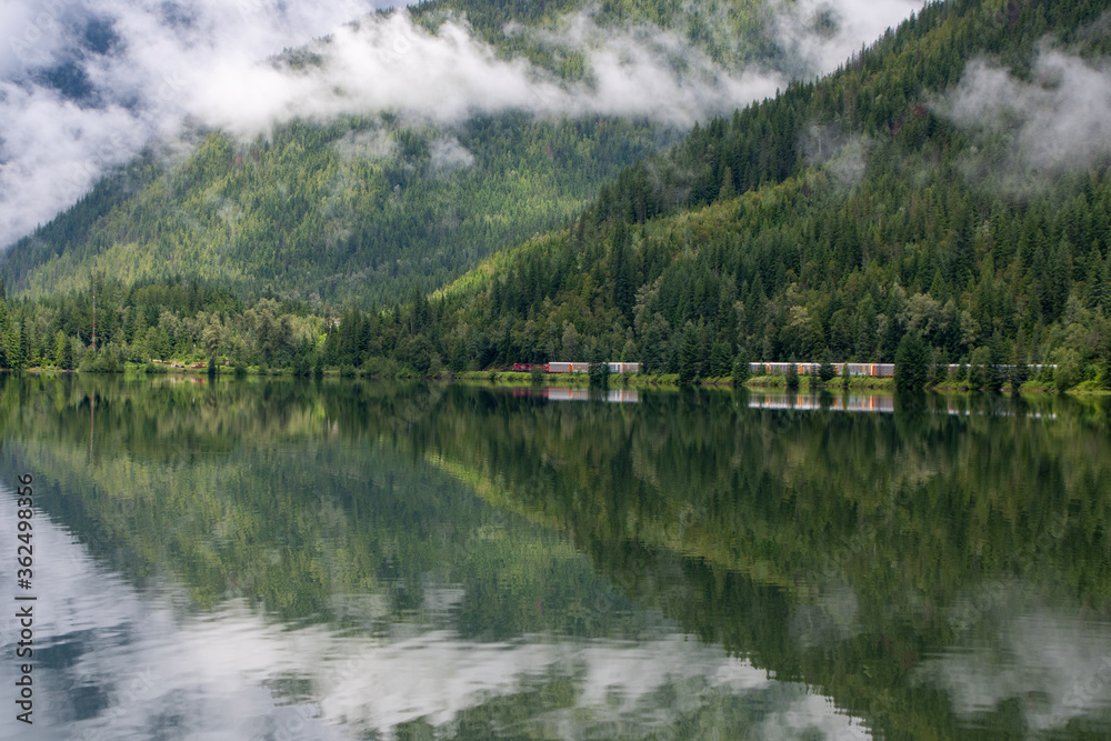 A picture of the mountains and passing freight train being symmetrically reflected on the surface of a lake.   BC Canada
