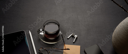 Modern office desk with digital supplies, coffee cup, notepad, glasses and decoration on black leather table