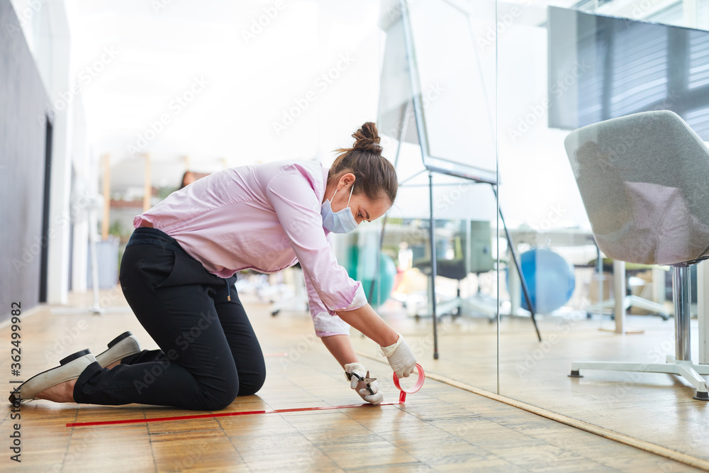 Obraz premium Woman marks floor with tape for keeping distance in the office