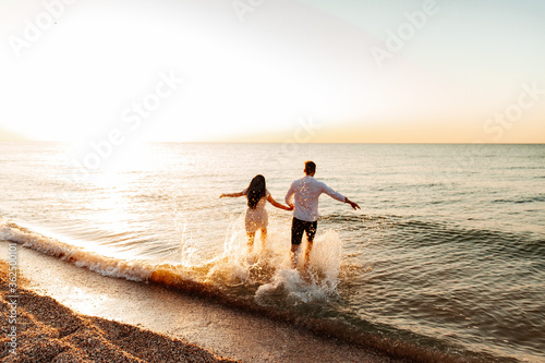Loving couple in white clothes during a honeymoon at sea walk on the sand at a photoshoot Love Story, ocean coast, beach