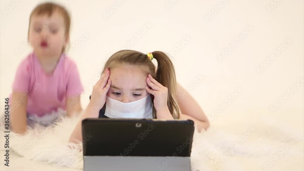 epidemic: a child in a medical mask to learn remotely. a girl on sick leave behind a laptop epidemic: a child in a medical mask to learn remotely. a girl on sick leave behind a laptop