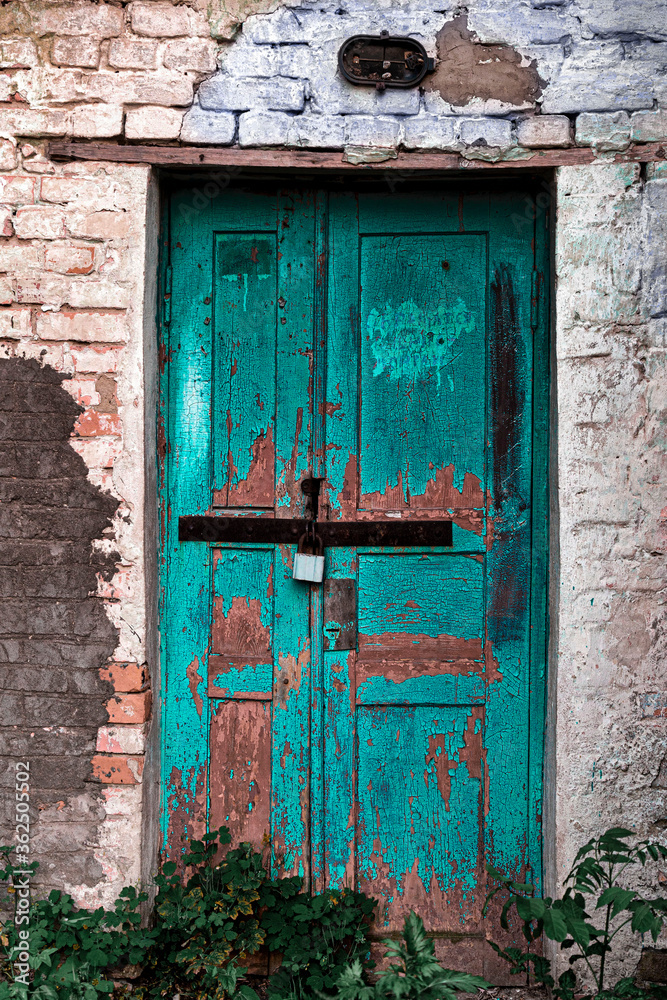 Old shabby wall facade of a brick building with wooden door in turquoise color. The concept of poverty, corruption and destruction.
