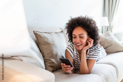 Lovely message from him. Attractive young woman looking at her smart phone and smiling while sitting on the sofa at home. Social networks. Young woman messaging on smartphone at home