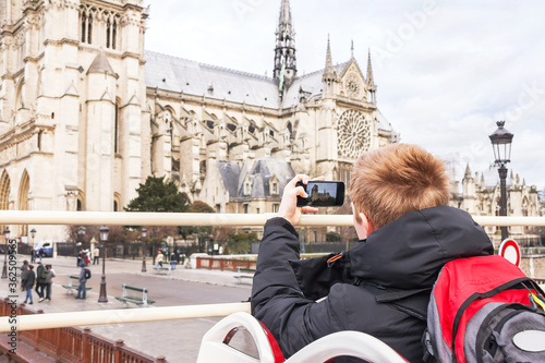 Teenager tourist is taking photo on cathedral of Notre Dame de Paris with mobile smart phone camera.